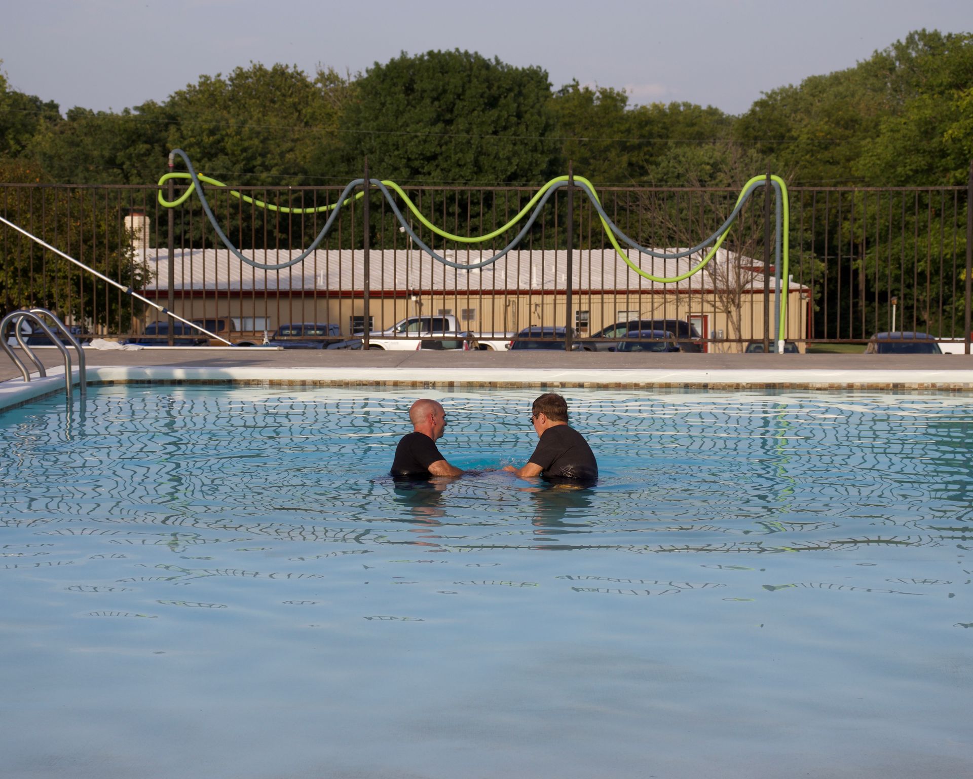 Two men are in a swimming pool talking to each other