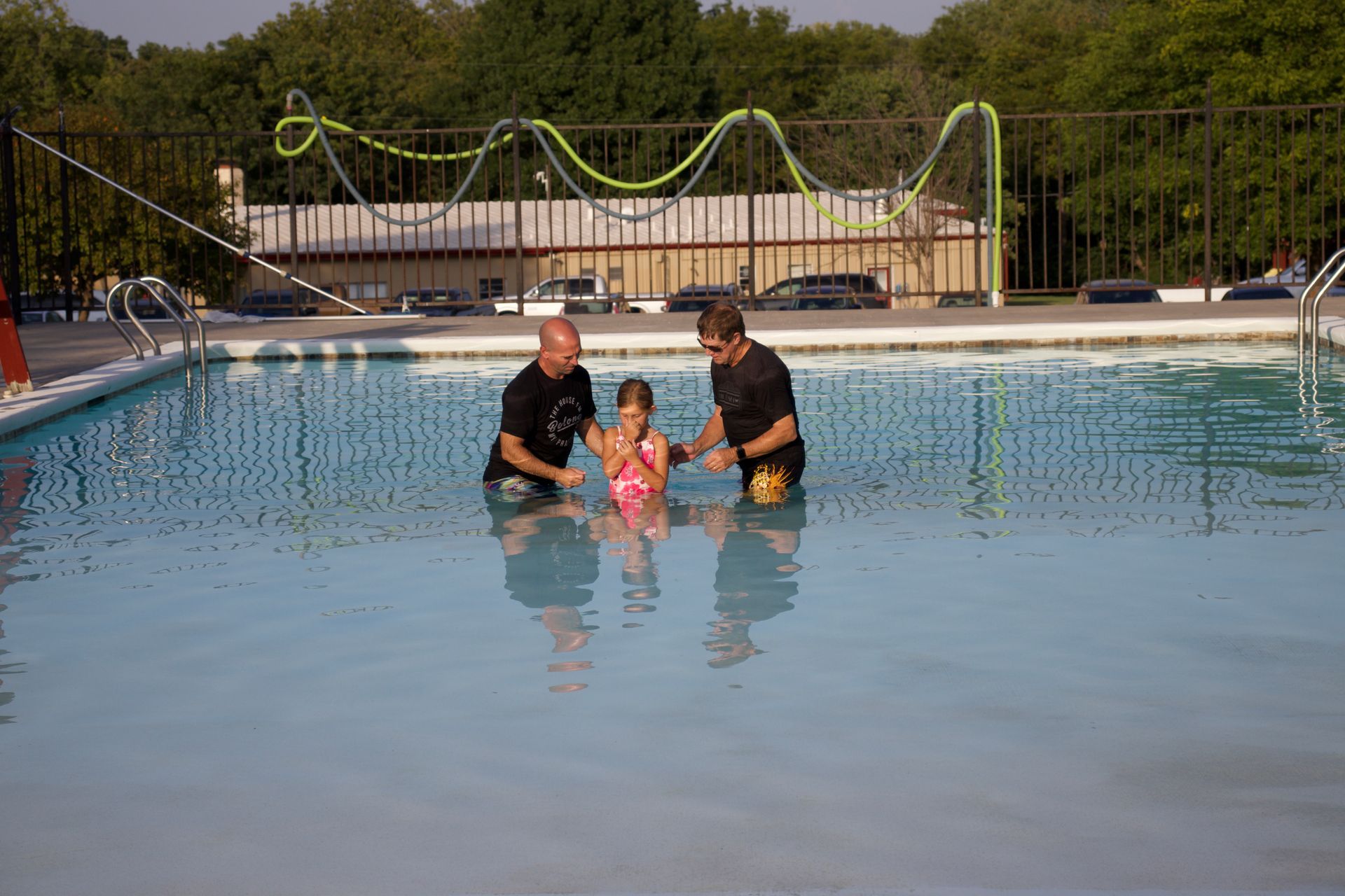 Two men are baptizing a little girl in a swimming pool.