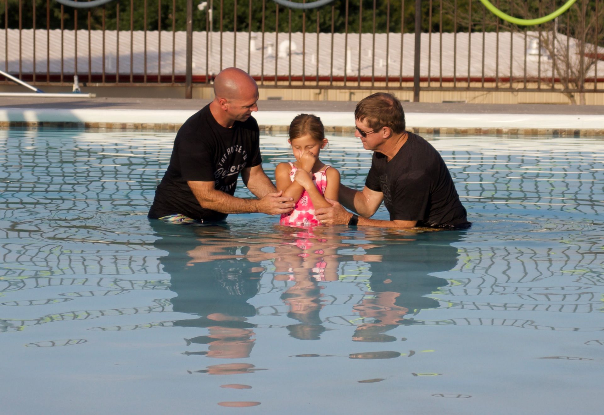 Two men are baptizing a little girl in a swimming pool