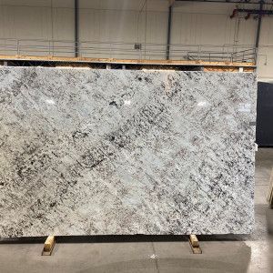 Large granite slab, mostly white with gray and black veining, resting on a wooden frame in a warehouse.