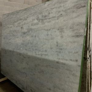 Gray and white marble slab with horizontal veining, stacked in a warehouse setting.