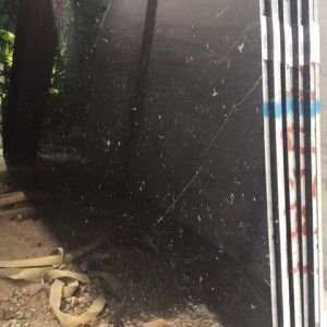 Black granite slab with visible cracks, standing outdoors next to a striped support.