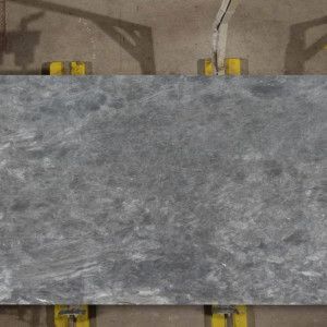 Overhead view of a large, grey marble slab with a textured appearance, supported by yellow blocks.