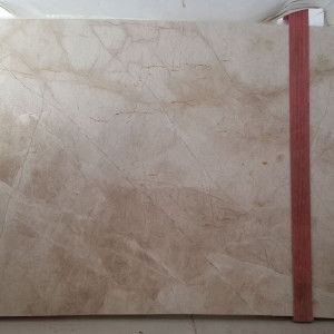 Tan-colored marble slab with light veining, held upright by a red strap.