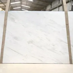 A large, white marble slab with gray veining, supported by wooden beams in a warehouse setting.