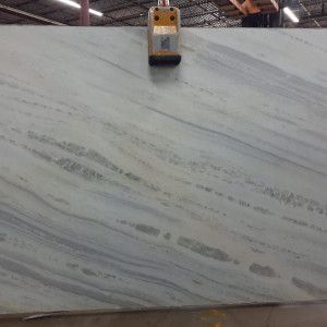 Large slab of white marble with grey and blue veining, held by industrial equipment.