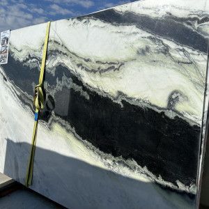 Large slab of black, green, and white marble, secured with a yellow strap; outdoors.