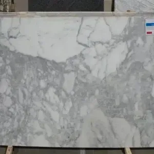 Large white marble slab with gray veining, on a wooden rack in a warehouse.