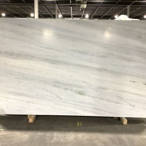 Large, white marble slab with gray veining, propped on wooden supports in a warehouse.