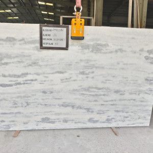 Large slab of white marble with gray veining, suspended by a crane. Sign attached.