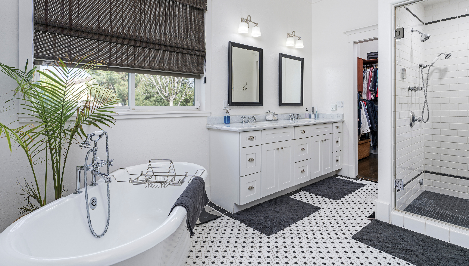 Spacious white bathroom with a standalone tub, double vanity, shower, and black and white patterned floor.