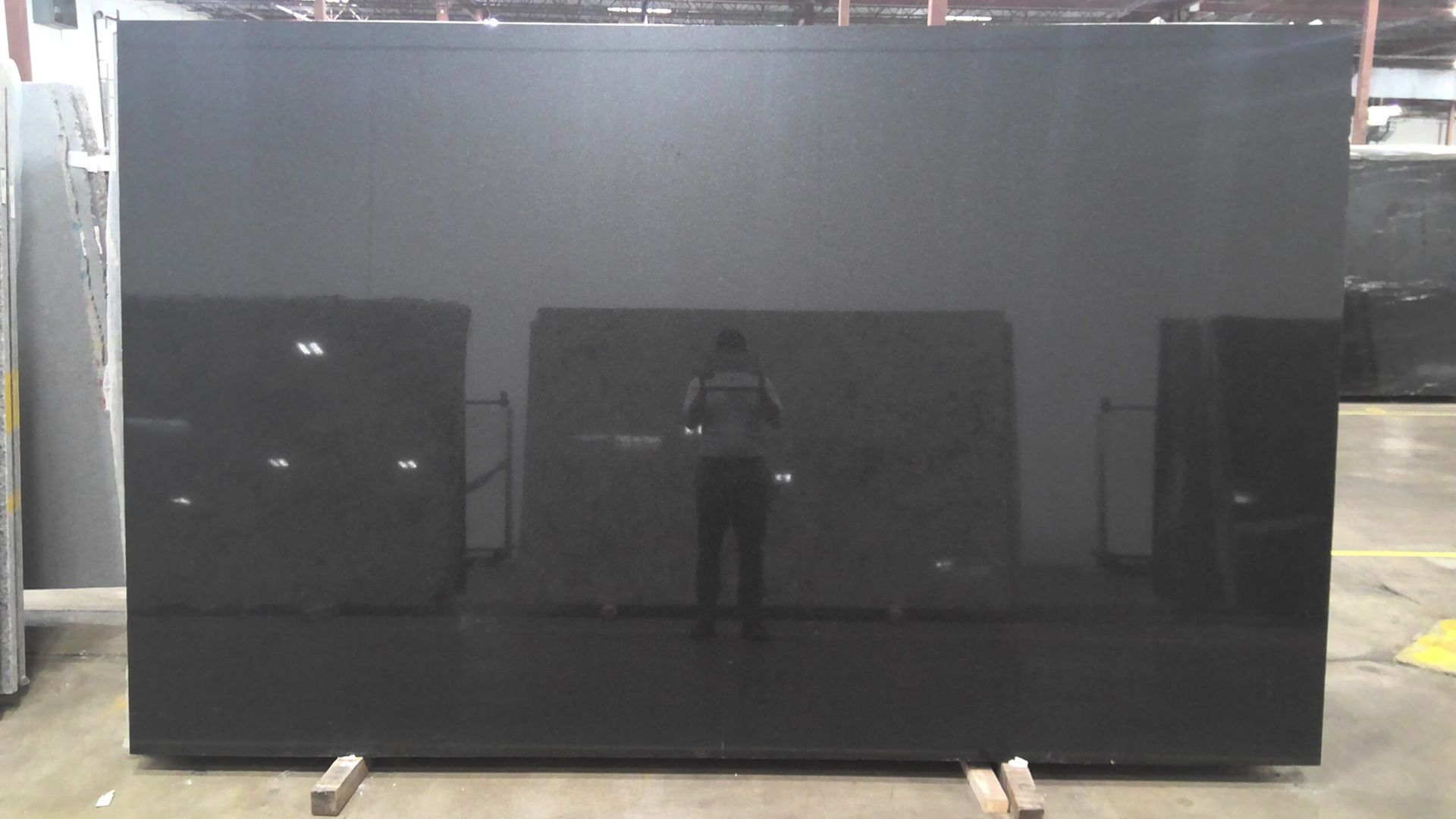Large black polished granite slab in a warehouse setting, reflecting the person taking the photo.