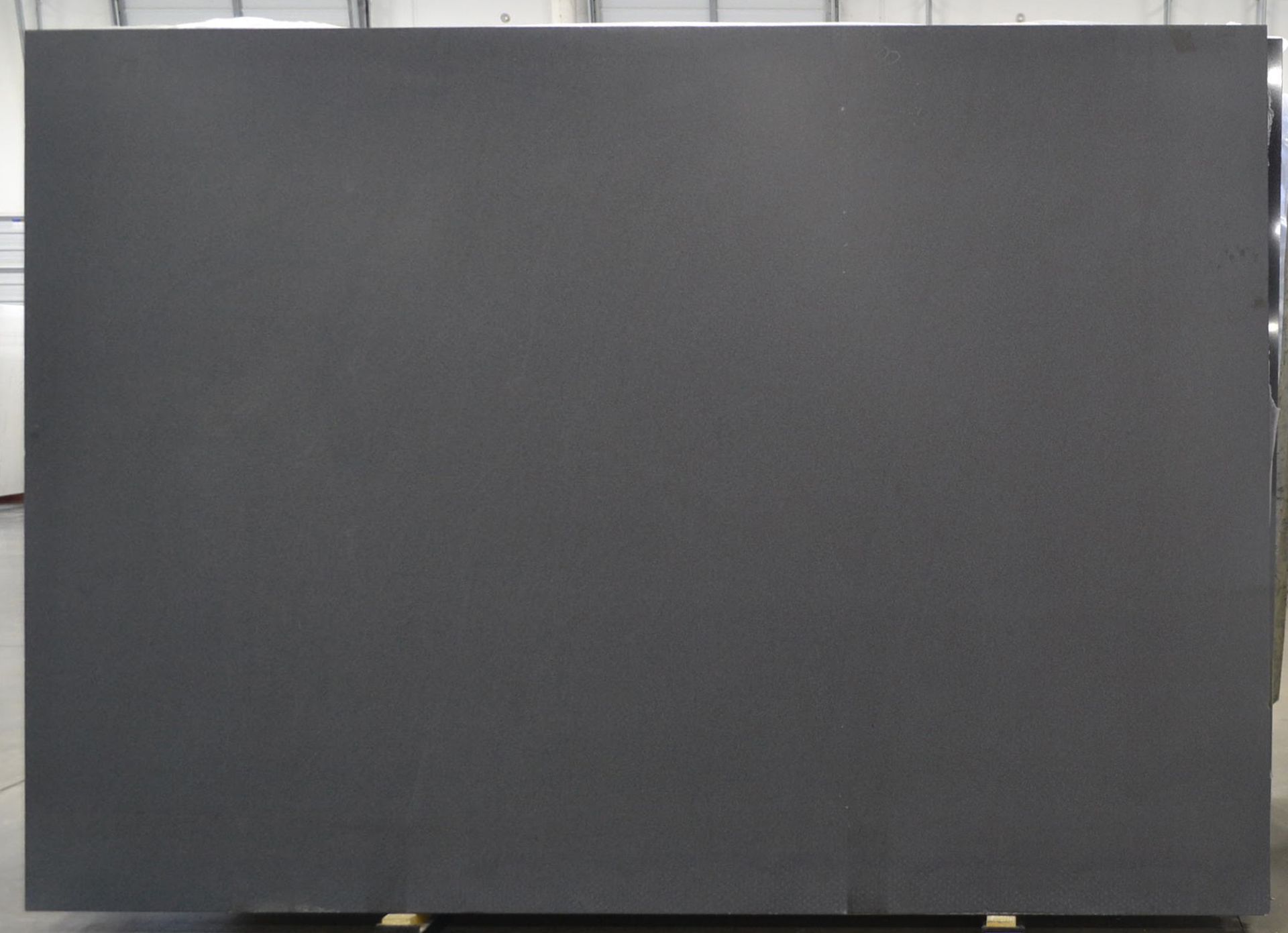 Large, dark gray stone slab, likely for countertop or surface, in a warehouse setting.