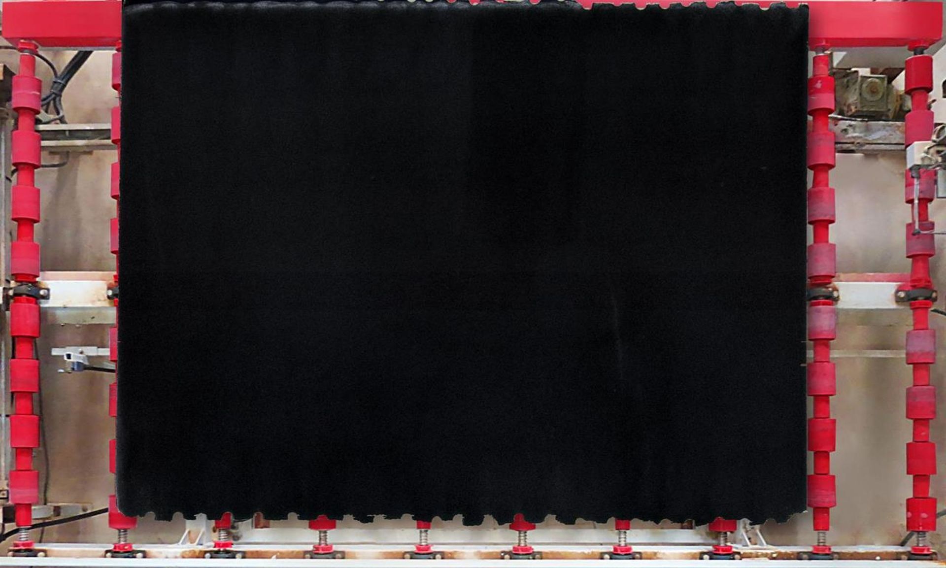 Black fabric being pressed in a red and white machine.