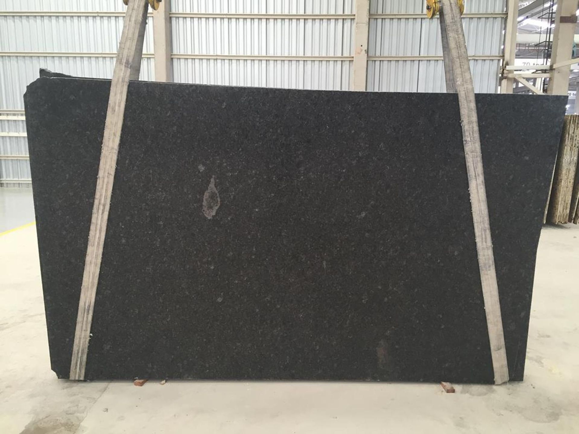 Large, black granite slab being lifted by wooden supports in a warehouse.