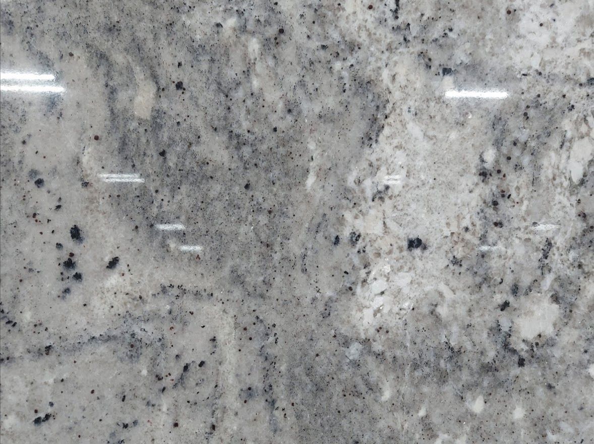 Close-up of a polished granite surface, primarily white with gray and black speckles and veining.