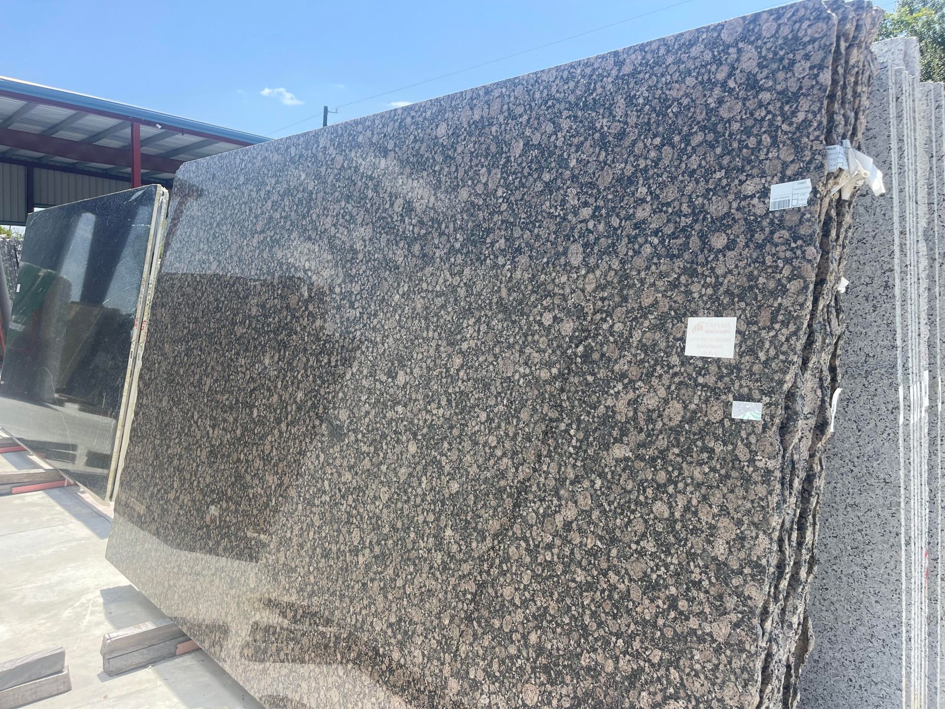 Granite slabs stacked outdoors, brown with flecks of lighter colors.
