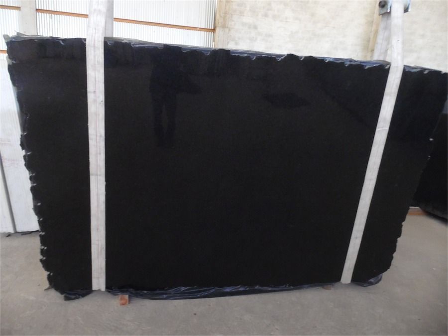 Large, polished black granite slab secured by white straps in a warehouse setting.