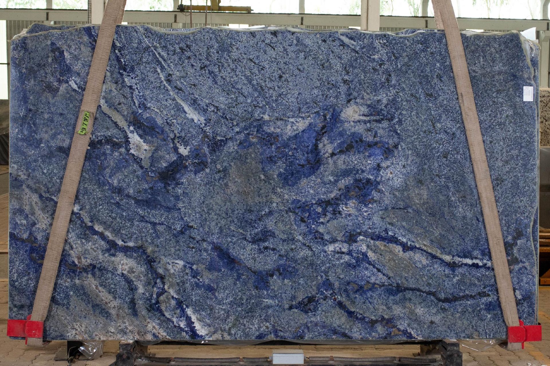 Large slab of blue granite, held by wooden straps, in a warehouse setting.