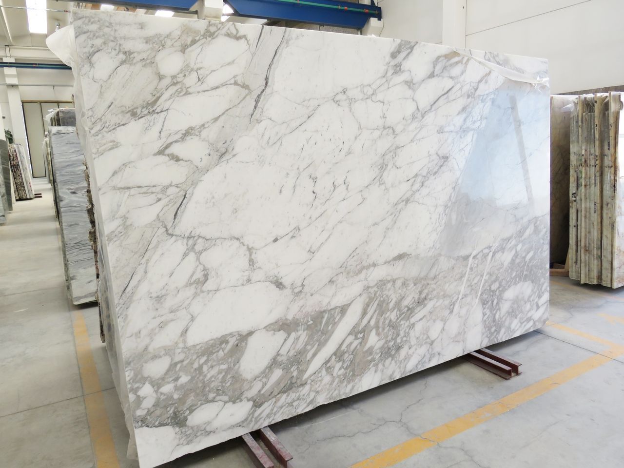 Large marble slab, white with gray veining, in a warehouse setting.