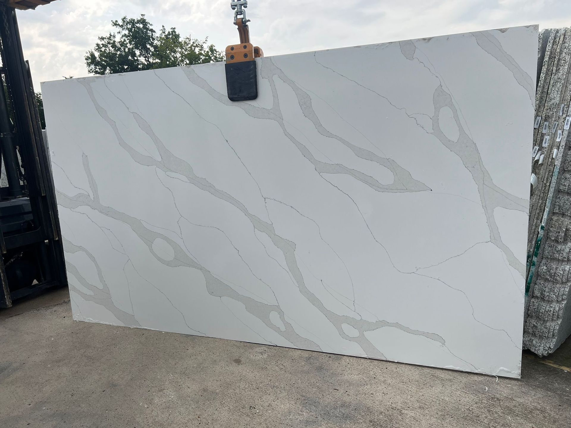 Large white quartz slab with grey veining, lifted by a forklift outdoors.