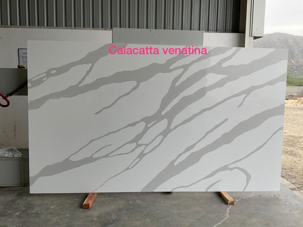 White Calacatta venatina quartz slab with gray veining, standing upright on a wooden rack.