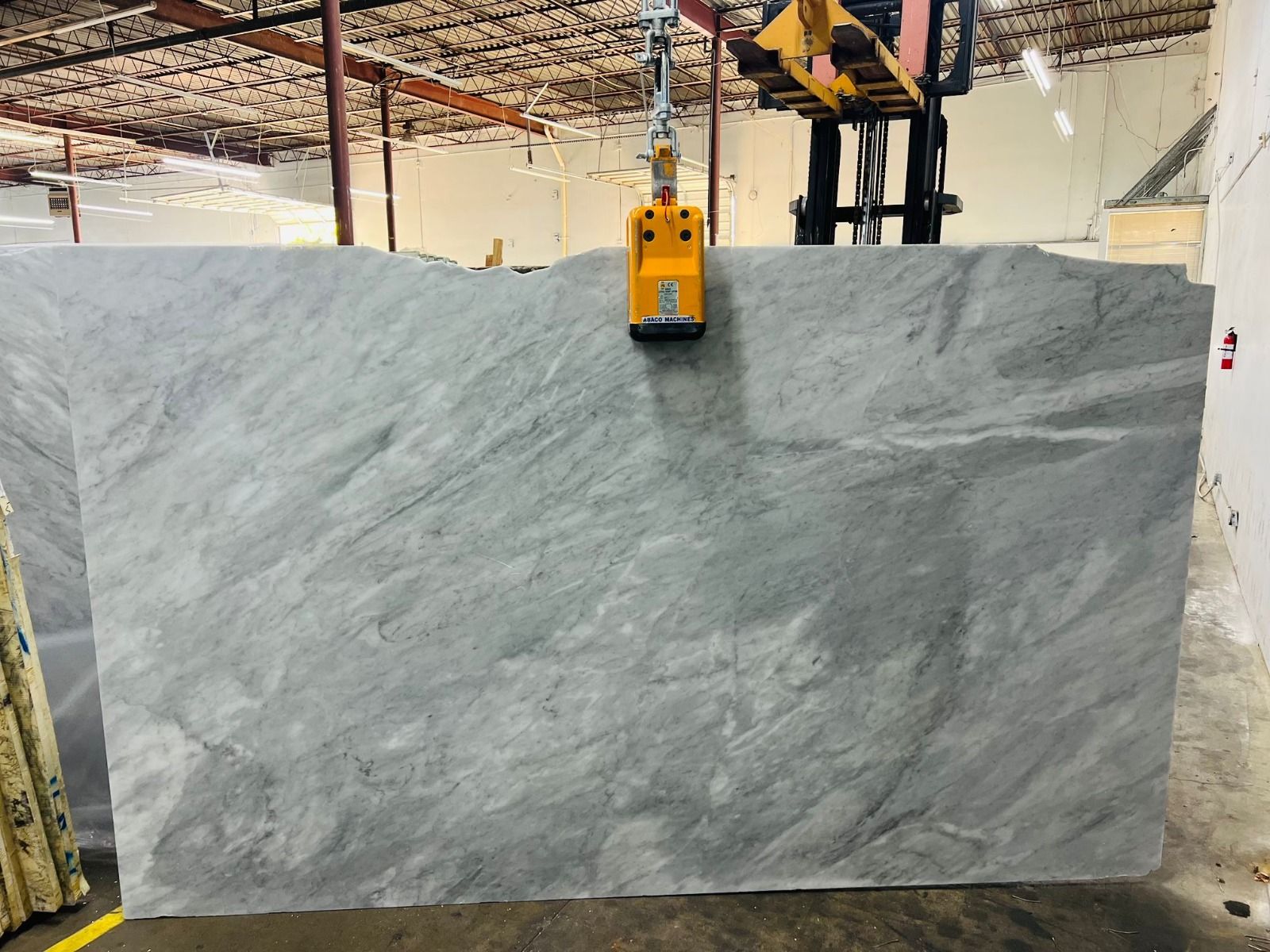 A large gray stone slab being lifted by a forklift in an industrial warehouse.