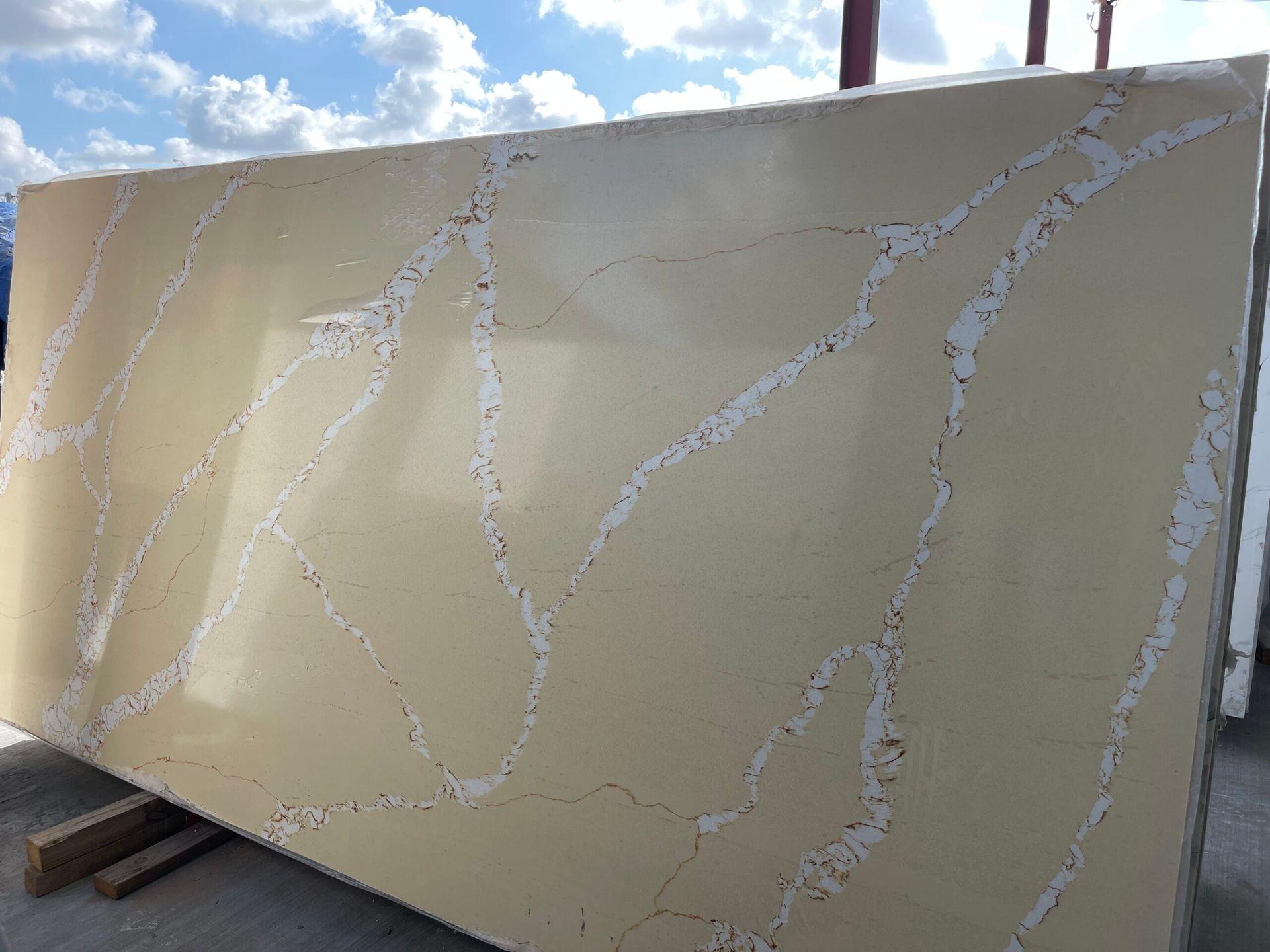 Beige quartz slab with white veining, displayed outdoors under a cloudy sky.