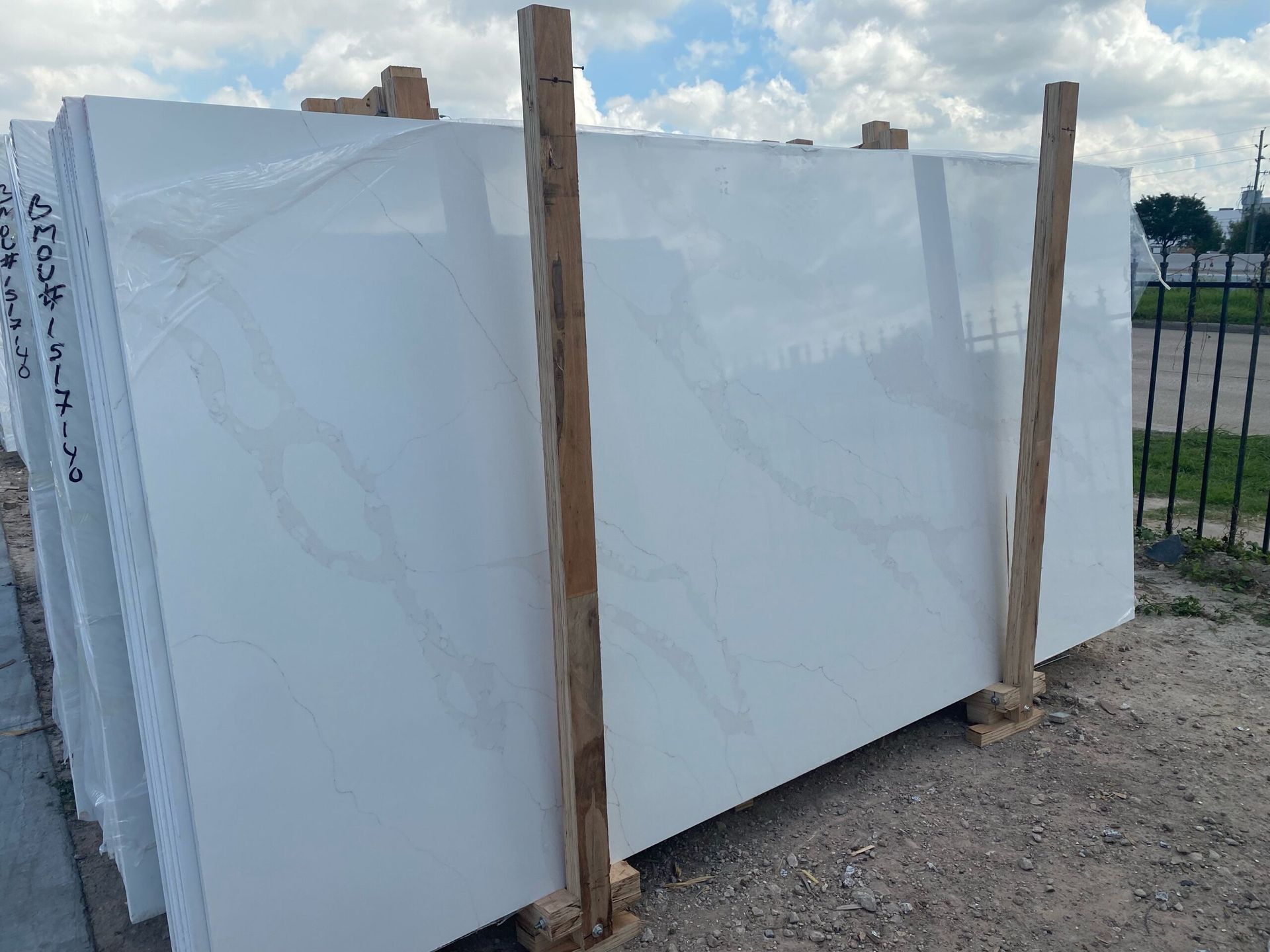 White quartz slabs stacked outside, supported by wooden beams, with a cloudy sky in the background.