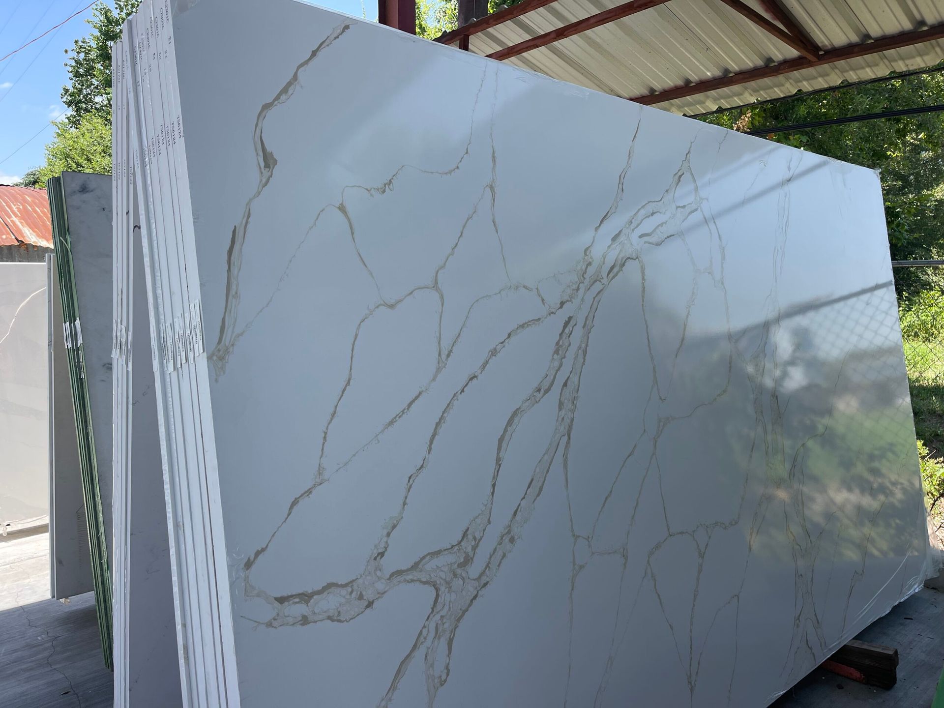White quartz countertop slab with gold veining, leaning against other slabs outside.