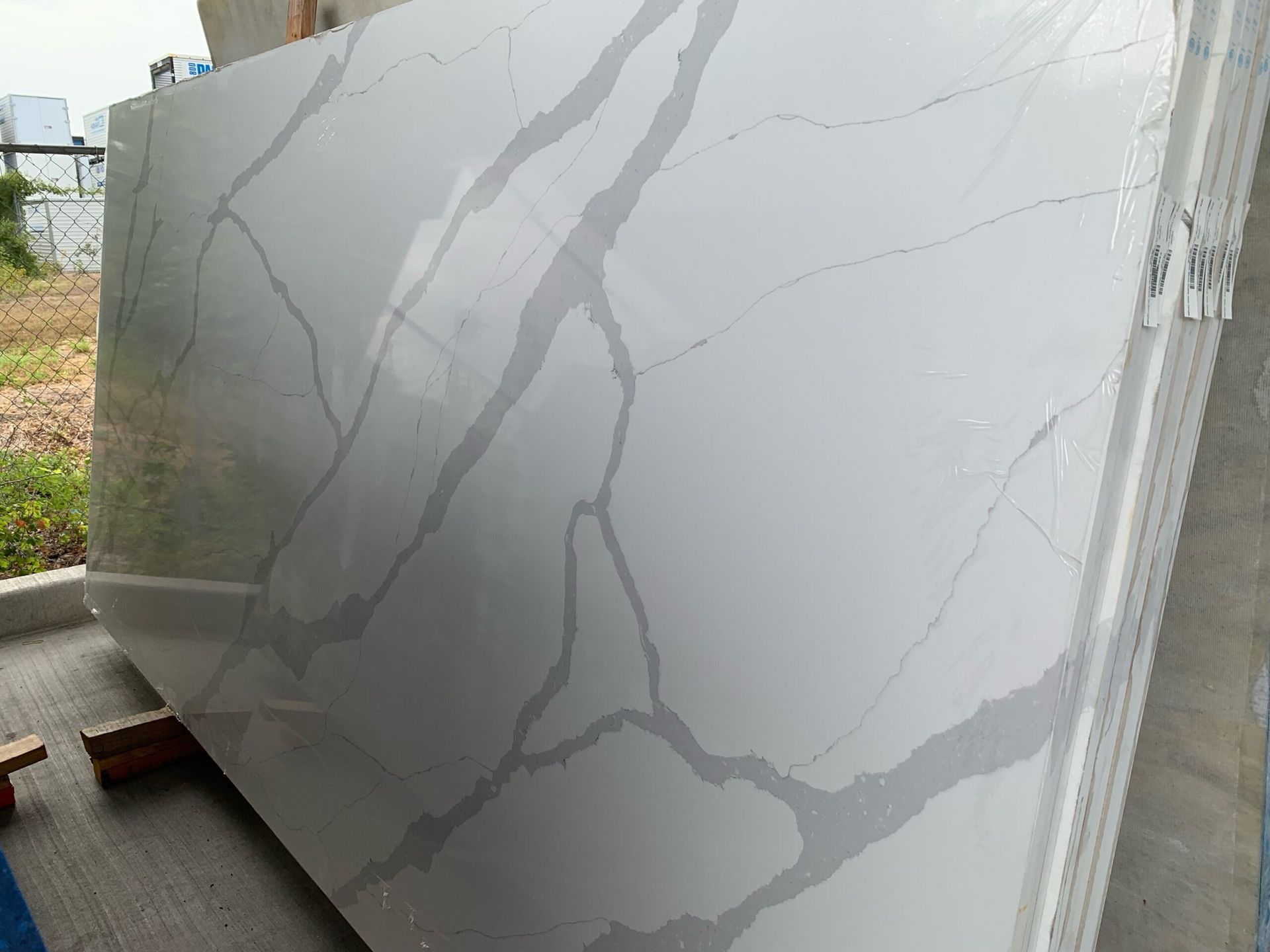 White quartz slab with grey veining, leaning against other slabs outdoors.