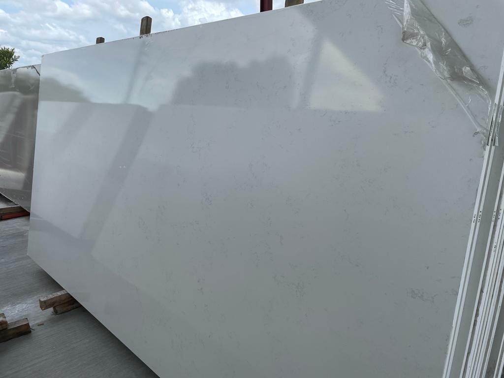 Large, light gray quartz slab outdoors, leaning against a rack, plastic wrap on edge.