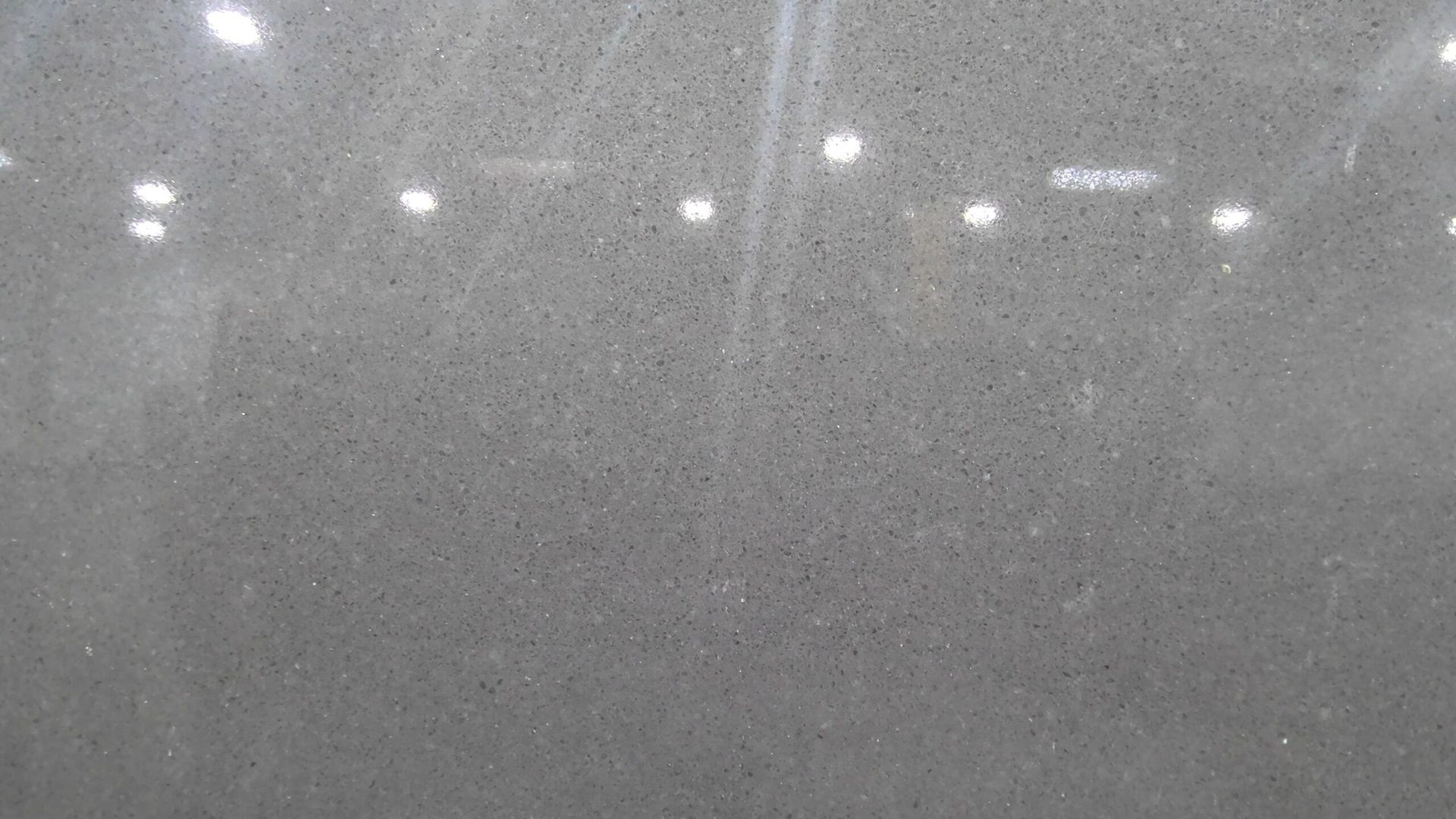 Gray stone surface with small speckled patterns. Reflective, with bright overhead lights.