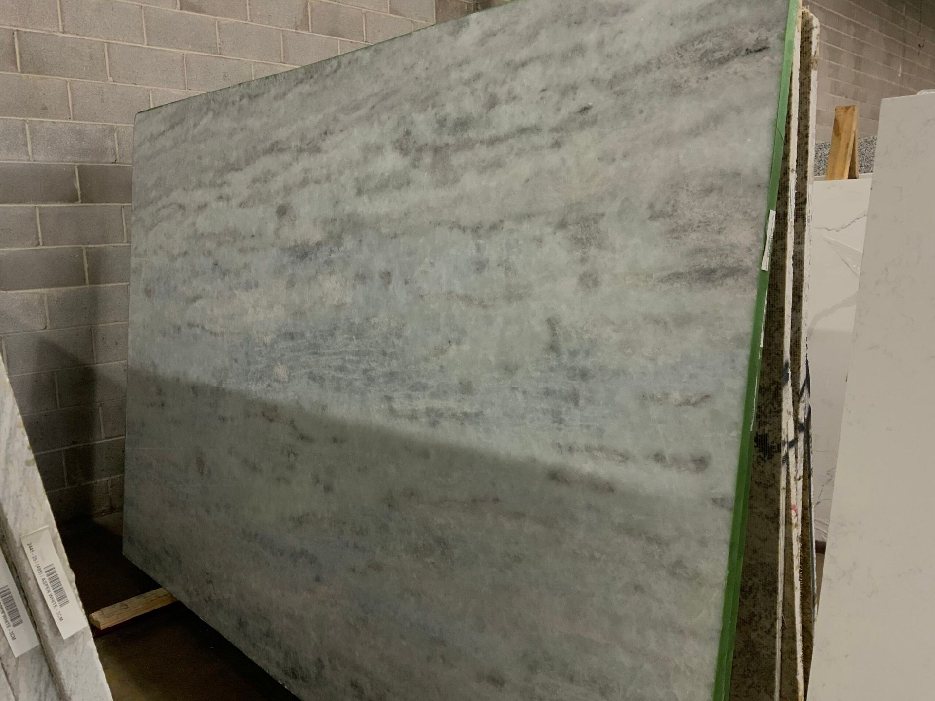Large slab of gray and white marble with veining, leaning against other slabs in a warehouse.