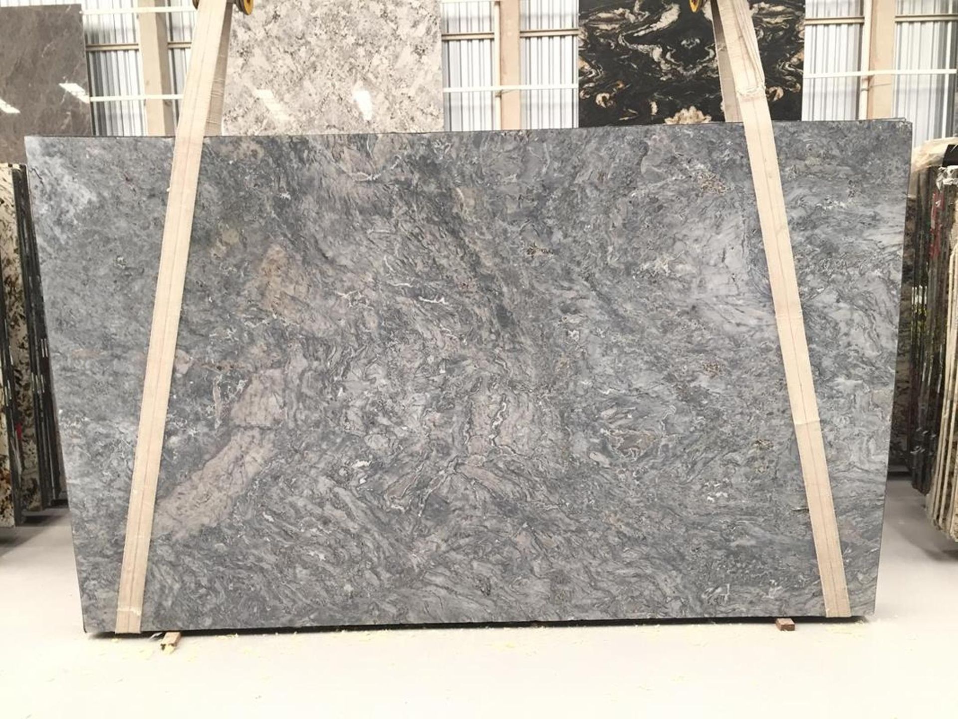 Large gray granite slab with swirling patterns, held upright by wooden supports in a showroom.