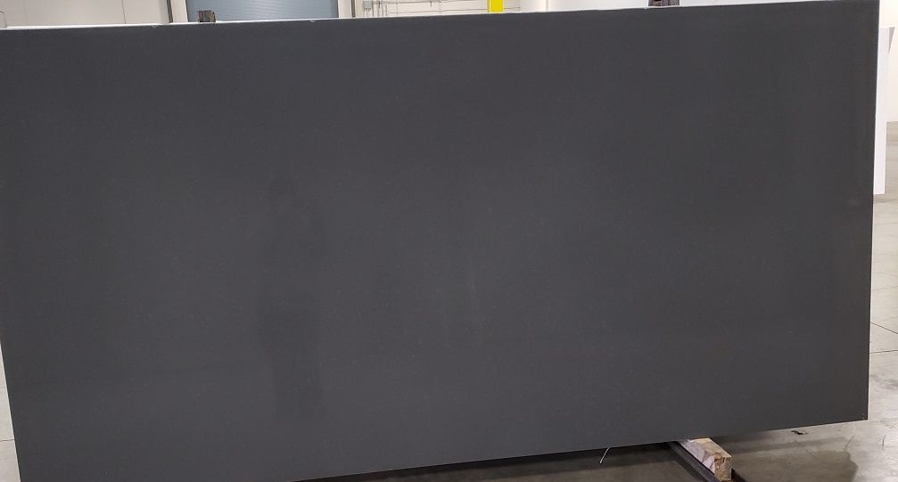 Large, dark gray stone slab, possibly countertop material, in a warehouse setting.