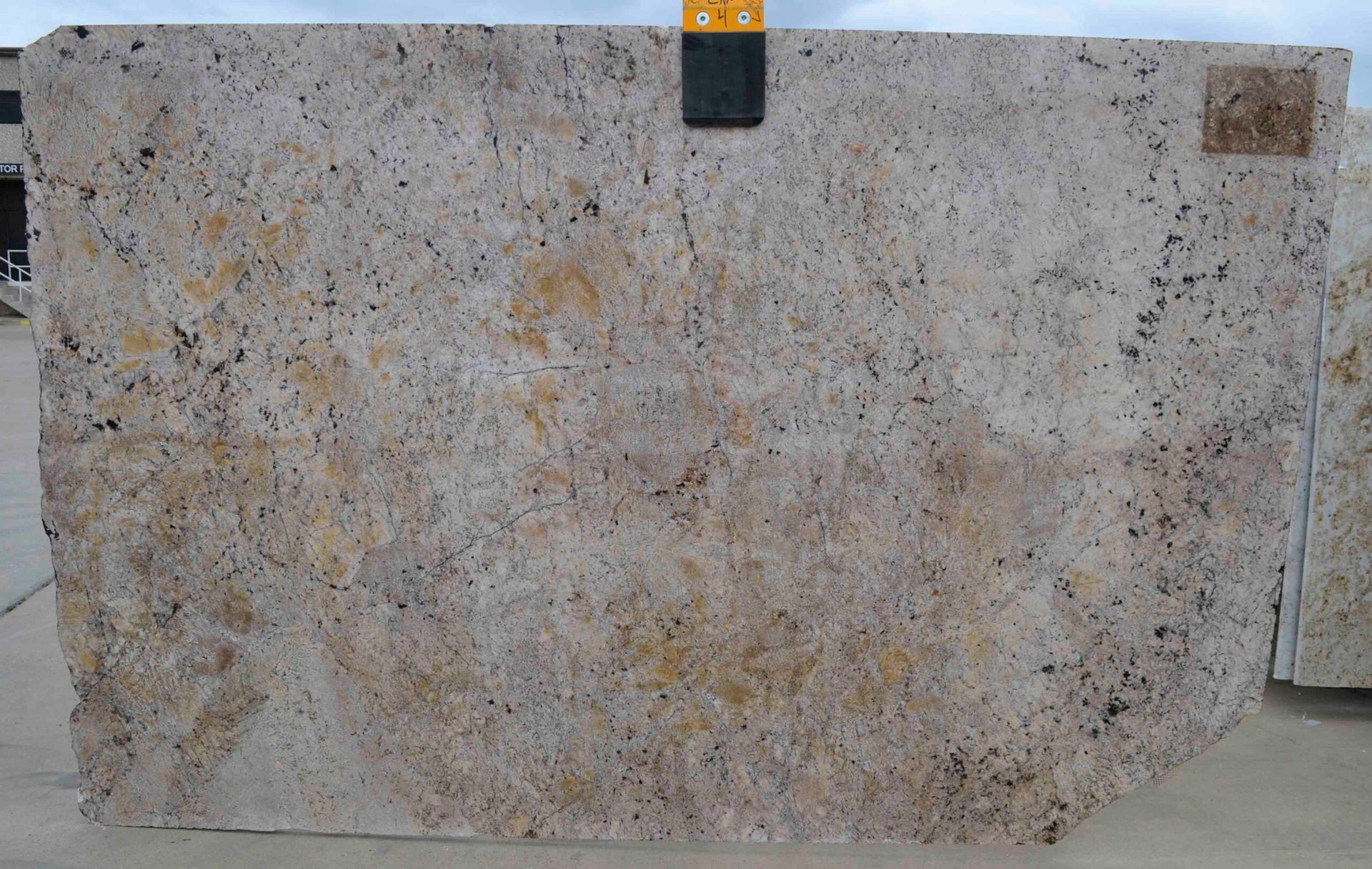 Light-colored granite slab with brown, black, and yellow specks. A black measuring tool rests on top.