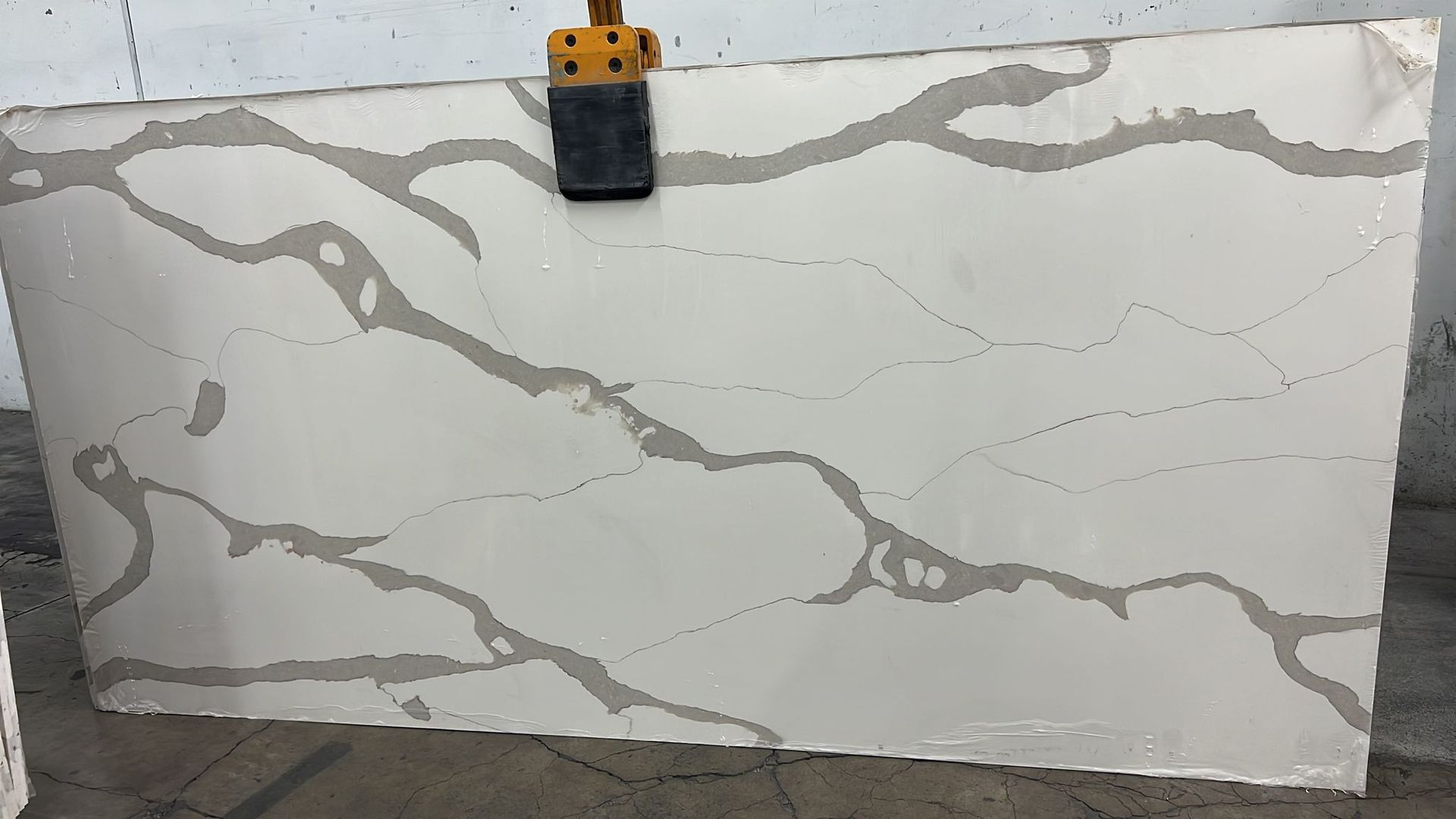 A large white quartz slab with gray veining, held by a clamp, indoors.