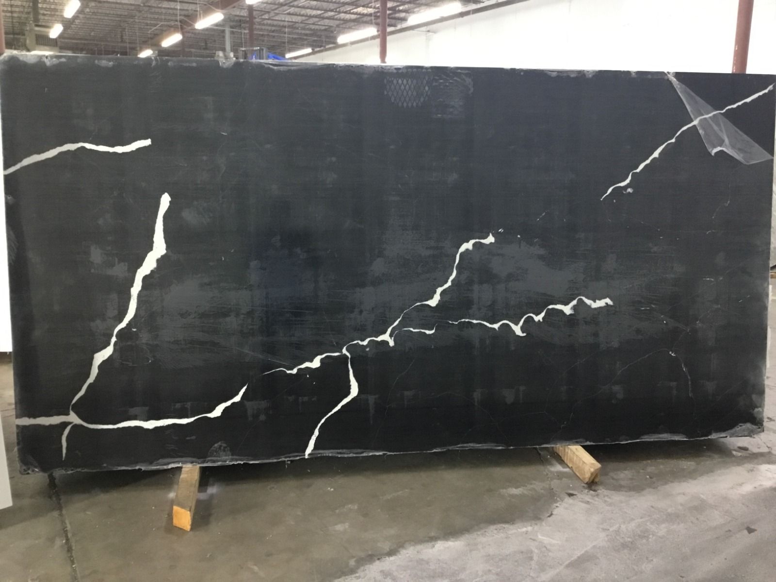 Large, dark black countertop with white veining, supported by wooden beams, in a warehouse.