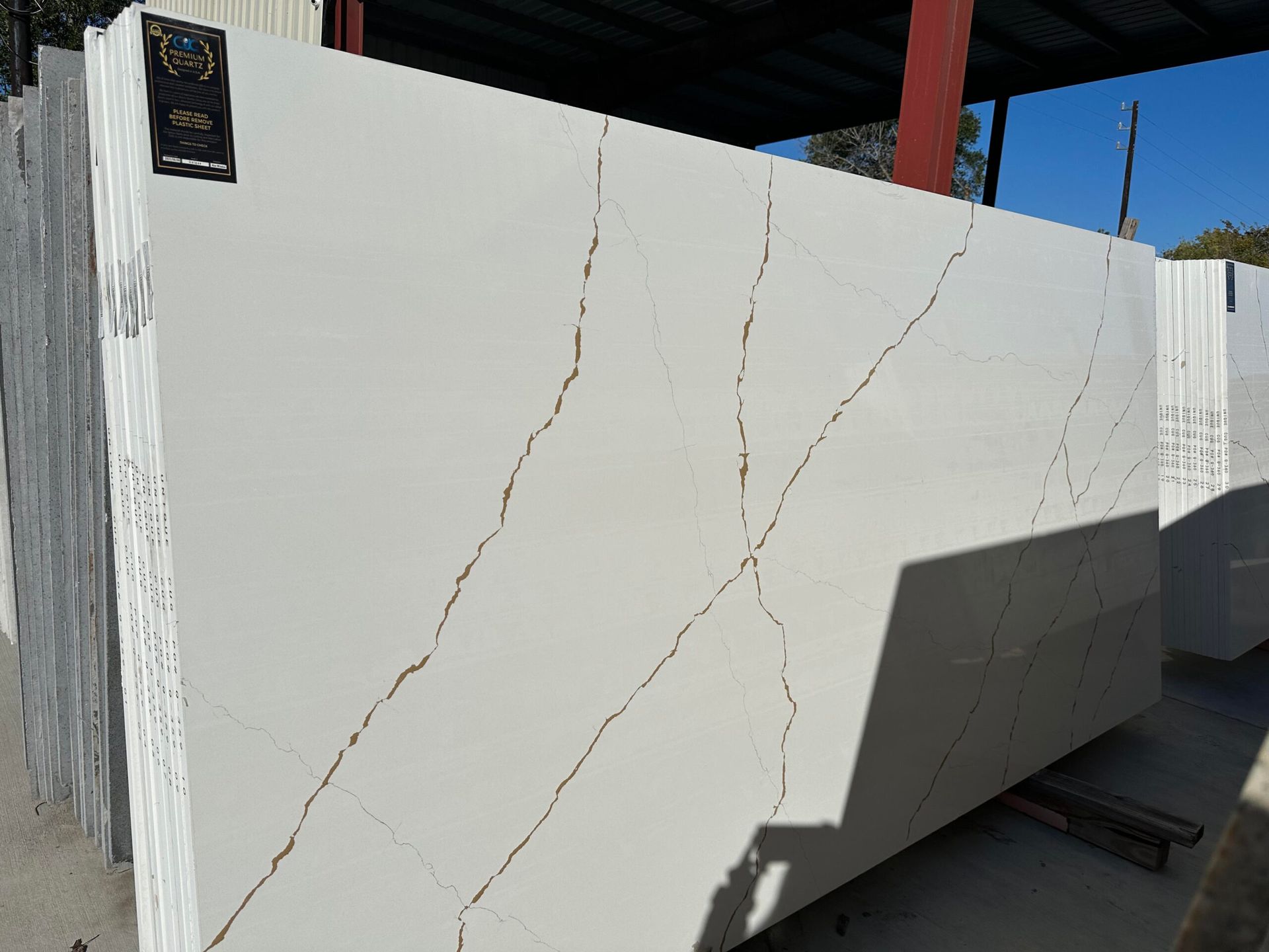 Large white quartz slabs with golden veining, stacked outdoors.