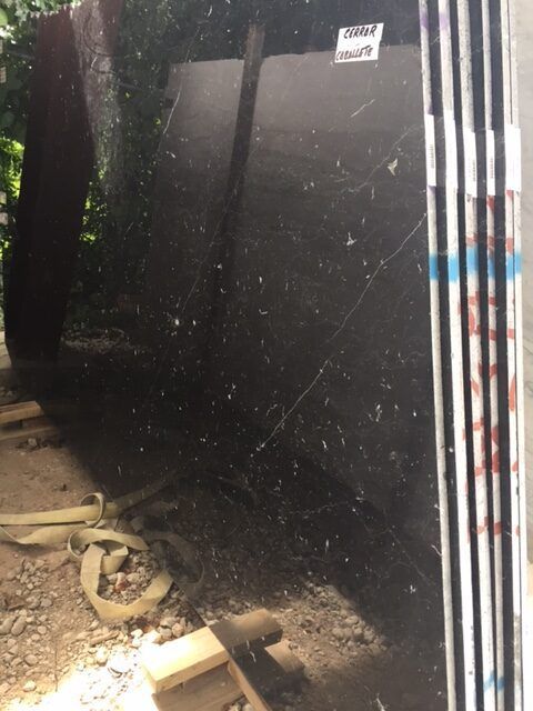 Black granite slabs stacked on a wood frame. White label, blue/red tape on the edges. Outdoors, ground level.