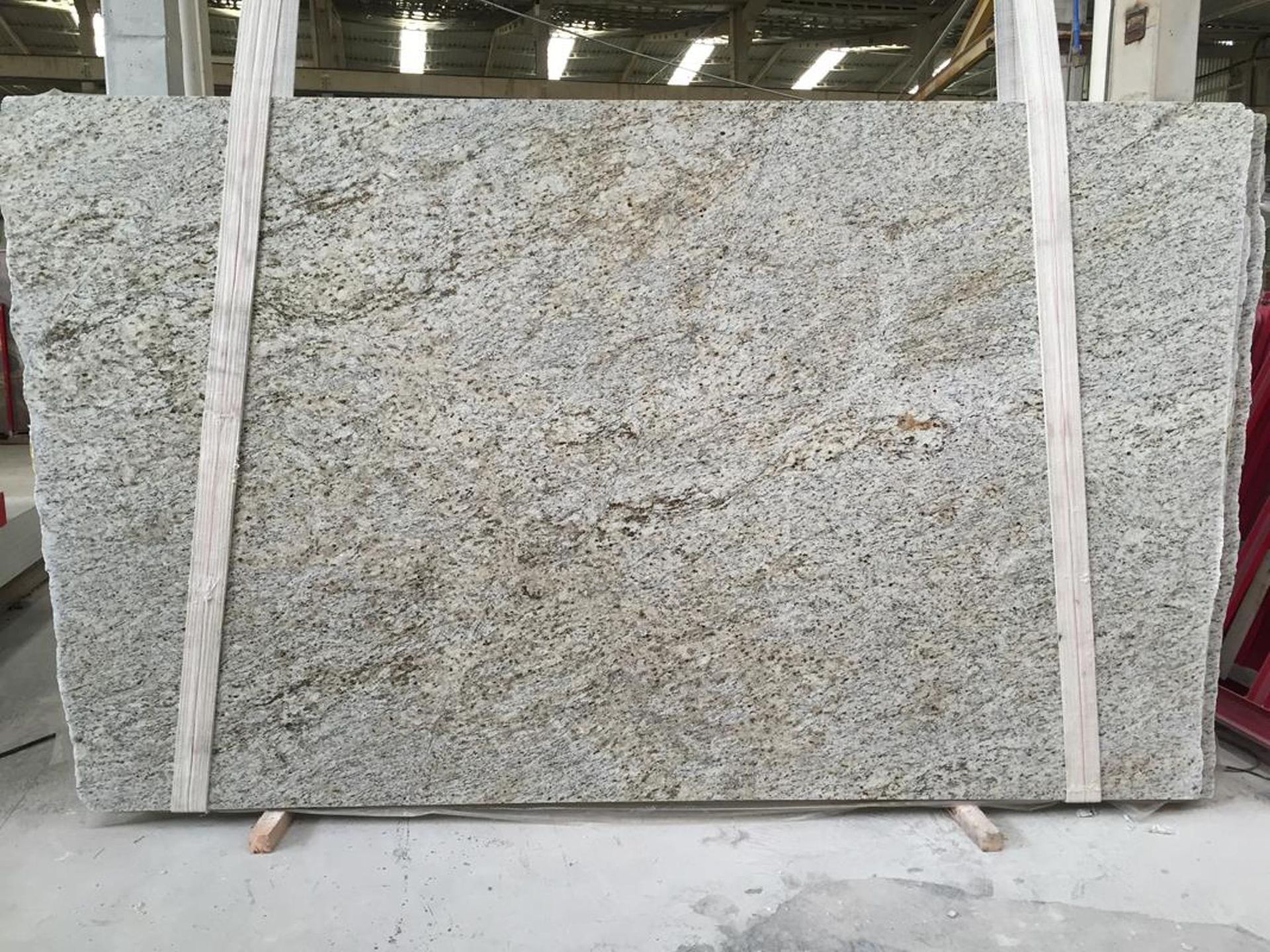 A large granite slab, pale grey with brown veining, displayed on wooden supports.