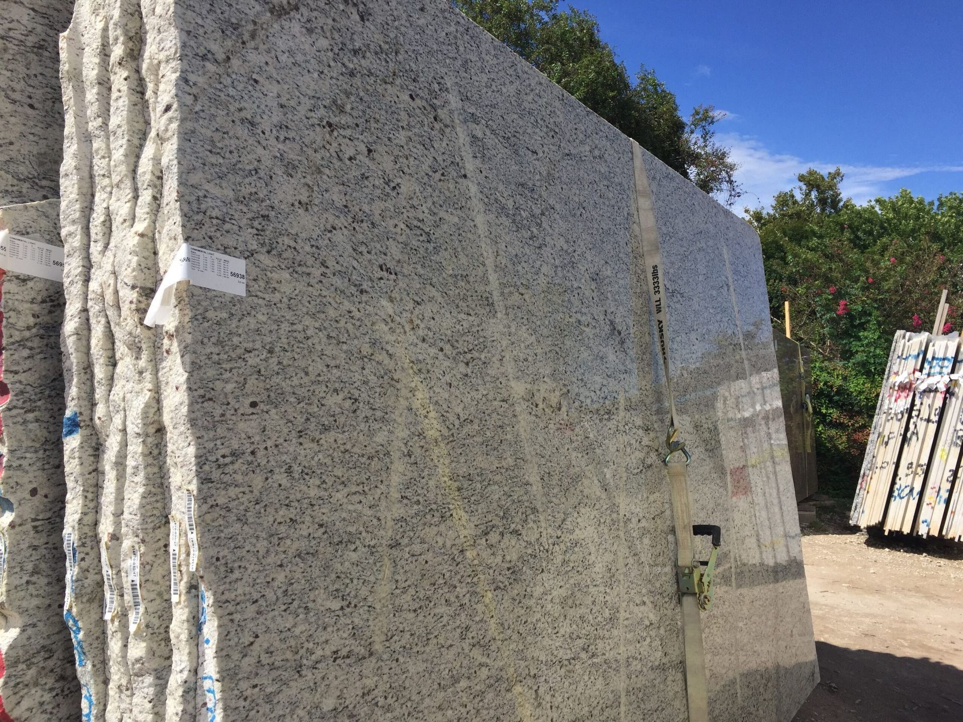 Stack of light granite slabs with speckled patterns outdoors against a blue sky.