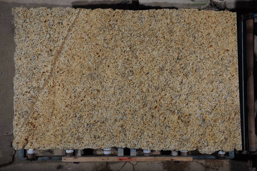 Tan granite slab on a metal rack, showing a coarse, textured surface with various shades.