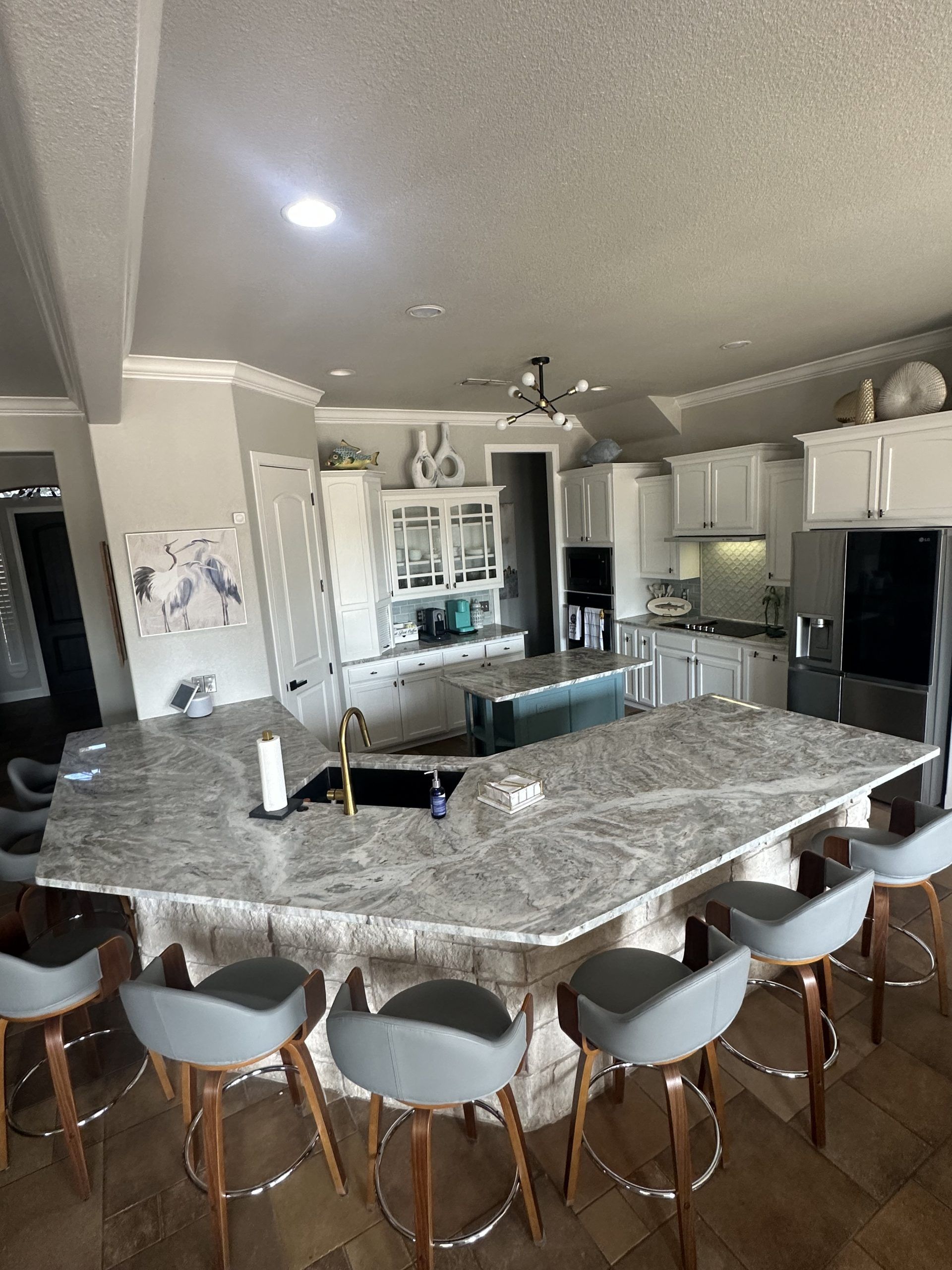 Modern kitchen with large granite island, bar stools, white cabinets, and stainless steel appliances.