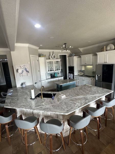 Kitchen with large granite island, white cabinets, and gray bar stools.