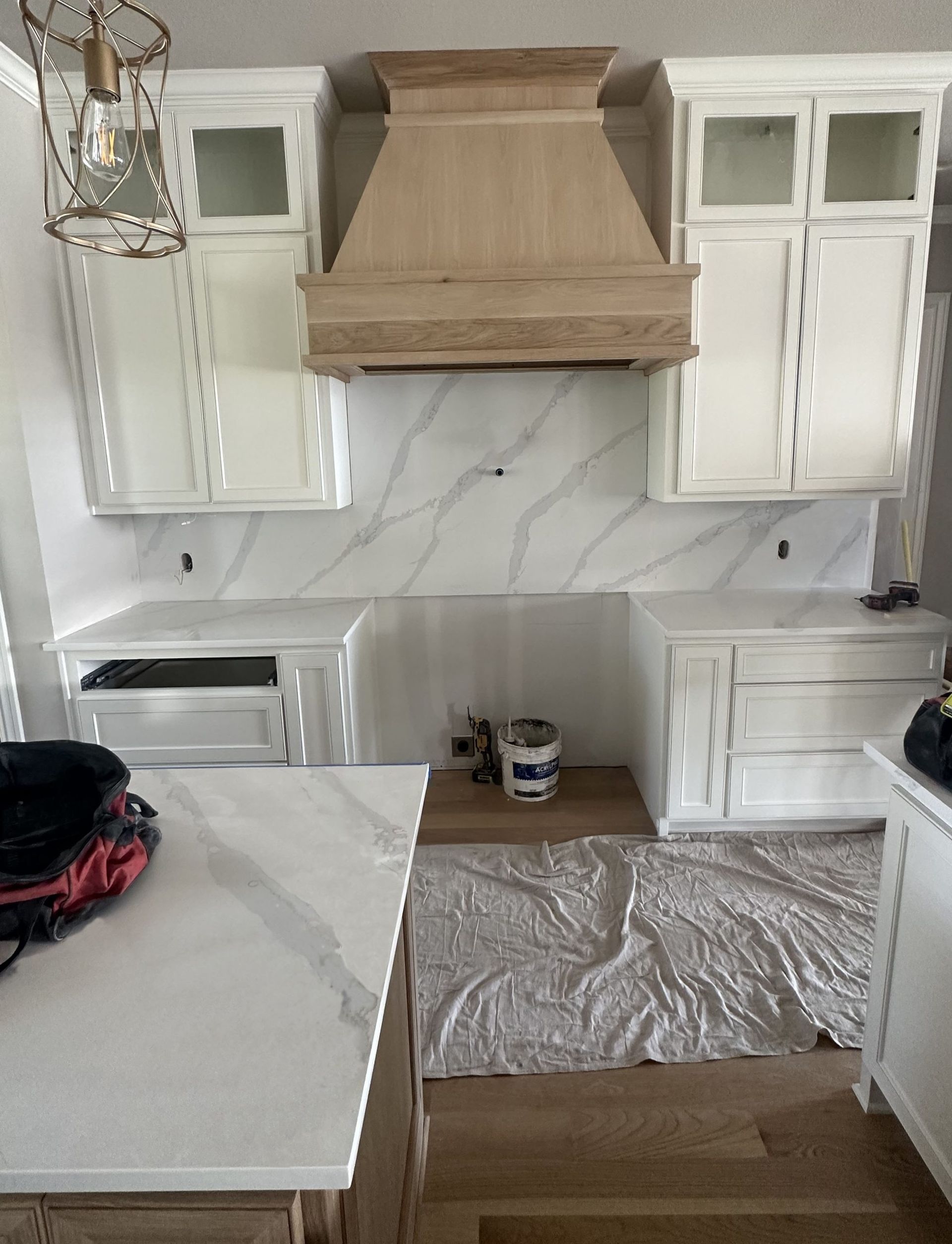 White kitchen cabinets with wood range hood and marble backsplash.