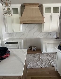 White kitchen with marble backsplash, wood vent hood, and white cabinets.