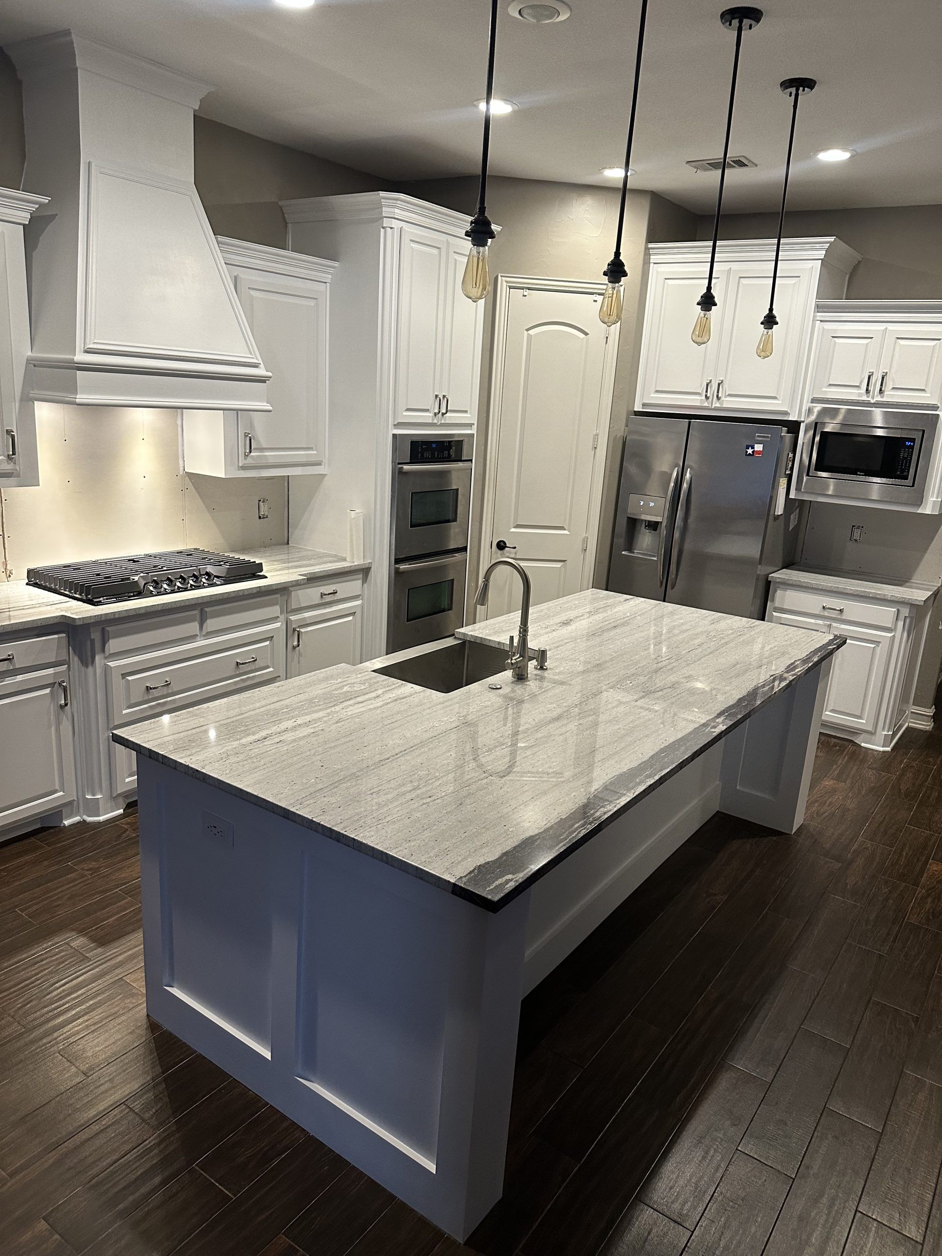 White kitchen with island, granite countertop, stainless steel appliances, dark wood floor.