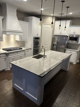 White kitchen with an island, granite countertop, and dark wood floor.